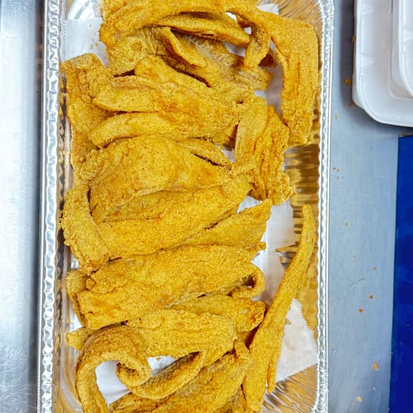 Golden-brown fried fish fillets, likely catfish, piled in a foil pan from M&M Chicken & Fish.