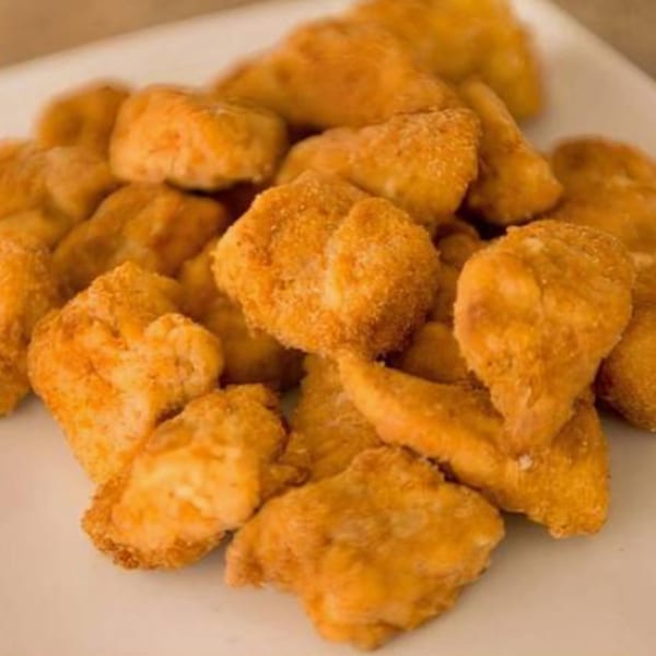 A close-up of a pile of golden-brown fried chicken pieces on a white plate.