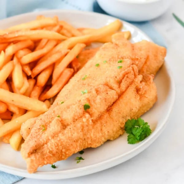 Golden-brown fried fish fillets and french fries on a white plate, garnished with parsley.