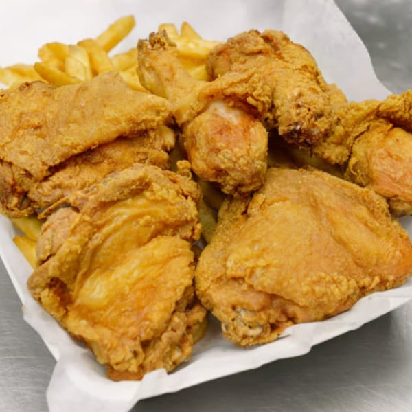A white paper container filled with golden-brown fried chicken pieces and french fries.
